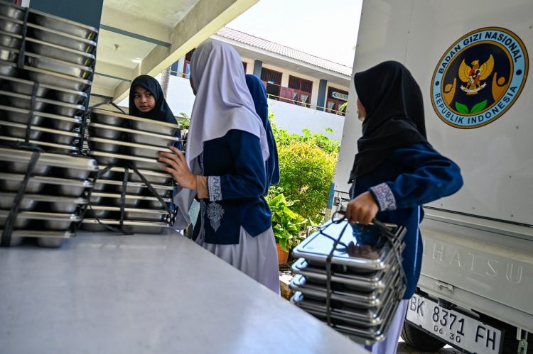 Students collect trays of food supplied by the Indonesian government's free meal programme at an elementary school in Banda Aceh on October 30, 2025. (Photo by CHAIDEER MAHYUDDIN / AFP)