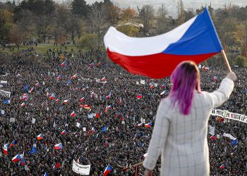 A woman waves a Czech flag from a roof as people take part in a large anti-government protest in Prague, Czech Republic, Saturday, Nov. 16, 2019. Czechs are rallying in big numbers to use the 30th anniversary of the pro-democratic Velvet Revolution and urge Prime Minister Andrej Babis to resign as peaceful protesters from all corners of the Czech Republic are attending the second massive protest opposing Babis at Letna park, a site of massive gatherings that significantly contributed to the fall of communism in 1989. (AP Photo/Petr David Josek)
