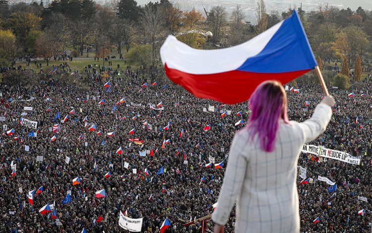 A woman waves a Czech flag from a roof as people take part in a large anti-government protest in Prague, Czech Republic, Saturday, Nov. 16, 2019. Czechs are rallying in big numbers to use the 30th anniversary of the pro-democratic Velvet Revolution and urge Prime Minister Andrej Babis to resign as peaceful protesters from all corners of the Czech Republic are attending the second massive protest opposing Babis at Letna park, a site of massive gatherings that significantly contributed to the fall of communism in 1989. (AP Photo/Petr David Josek)