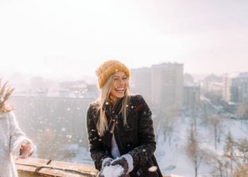 Young smiling woman enjoys snowy winter day on a rooftop terrace that overlooks the city