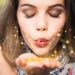 A young woman closing her eyes as she blows golden confetti from her hand, and makes a wish.