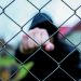 Aggressive  teenage boy showing hes fist behind wired fence at the correctional institute,  focus on the wired fence, conceptual image of juvenile delinquency .