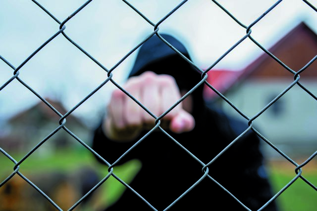 Aggressive teenage boy showing hes fist behind wired fence at the correctional institute, focus on the wired fence, conceptual image of juvenile delinquency .