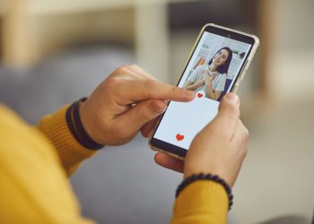 Dating app or site in mobile phone screen. Close up of a lonely man uses a smartphone to flip through women's profiles and presses a heart button with his finger. Banner or mockup website concept.