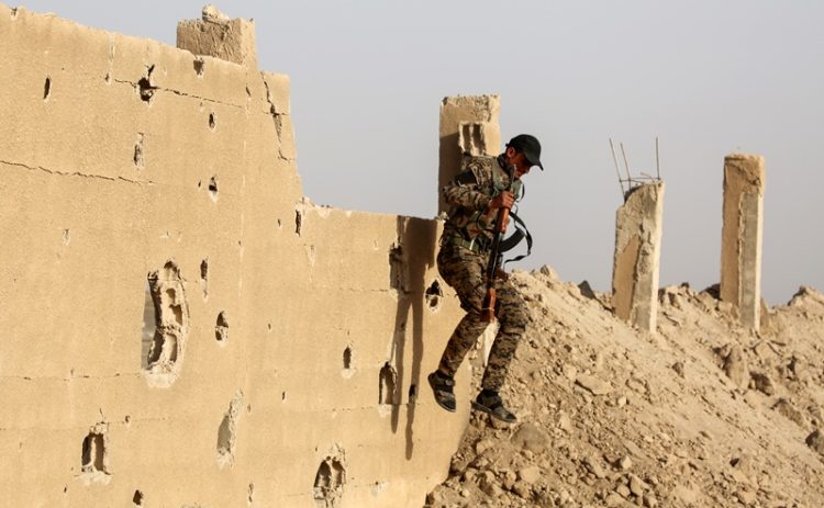 A member of the Kurdish People's Protection Units (YPG) jumps from a wall as he carries a Kalashnikov assault rifle in the town of al-Karamah, 26 kms from the Islamic State (IS) group bastion of Raqa, on May 10, 2017. / AFP PHOTO / DELIL SOULEIMAN
