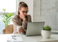 Young woman holding cup of coffee and looking at computer