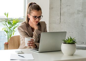Young woman holding cup of coffee and looking at computer