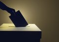 Silhouette of a hand putting a vote into the voting box on pale yellow background. Illustration of the concept of legislative election